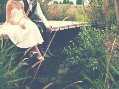 Bride and groom sitting together on a wooden bridge surrounded by greenery and wild planting