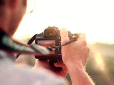 Photographer holding a DSLR camera and adjusting settings while shooting into the sunset