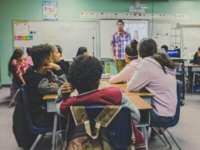 Teacher standing at the front of a classroom with students seated at desks facing him