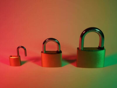 Three padlocks of increasing size, one open and two closed, lit with red and green lighting