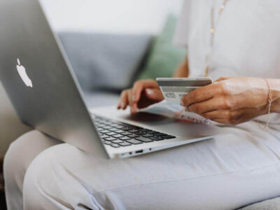 Woman sitting with a laptop on her knees holding a payment card while shopping online